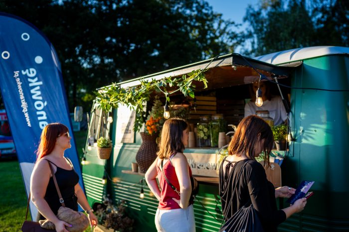 Na zdjęciu watertruck serwujący kranówkę i osoby czekające w kolejce po wodę. W tle chorągiewka z napisem #PijKranówkę. 