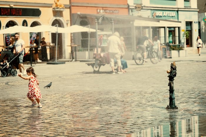 Na zdjęciu dziewczynka bawiąca się w mgiełce wodnej wydostającej się kurtyny wodnej zlokalizowanej w centrum Wrocławia, w rynku